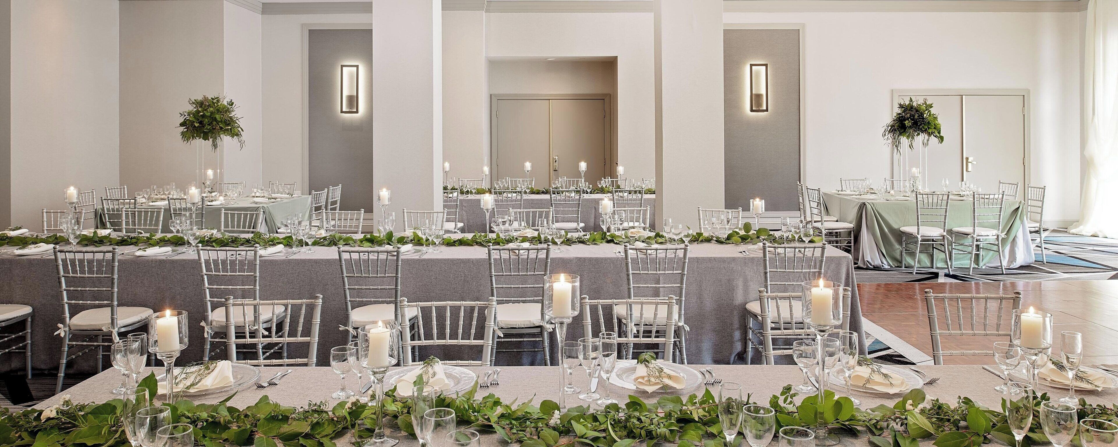Un amplio salón de banquetes con varias mesas redondas, cada una cubierta con manteles blancos, velas y cristalería.