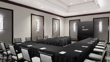 Een congreszaal van een Sheraton hotel met een lange tafel, stoelen en een groot scherm.