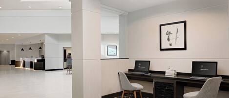 A modern hotel lobby with a reception desk, two computers, a framed artwork, and a patterned carpet.