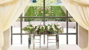 A table set for a wedding reception with white chairs and a floral centerpiece.