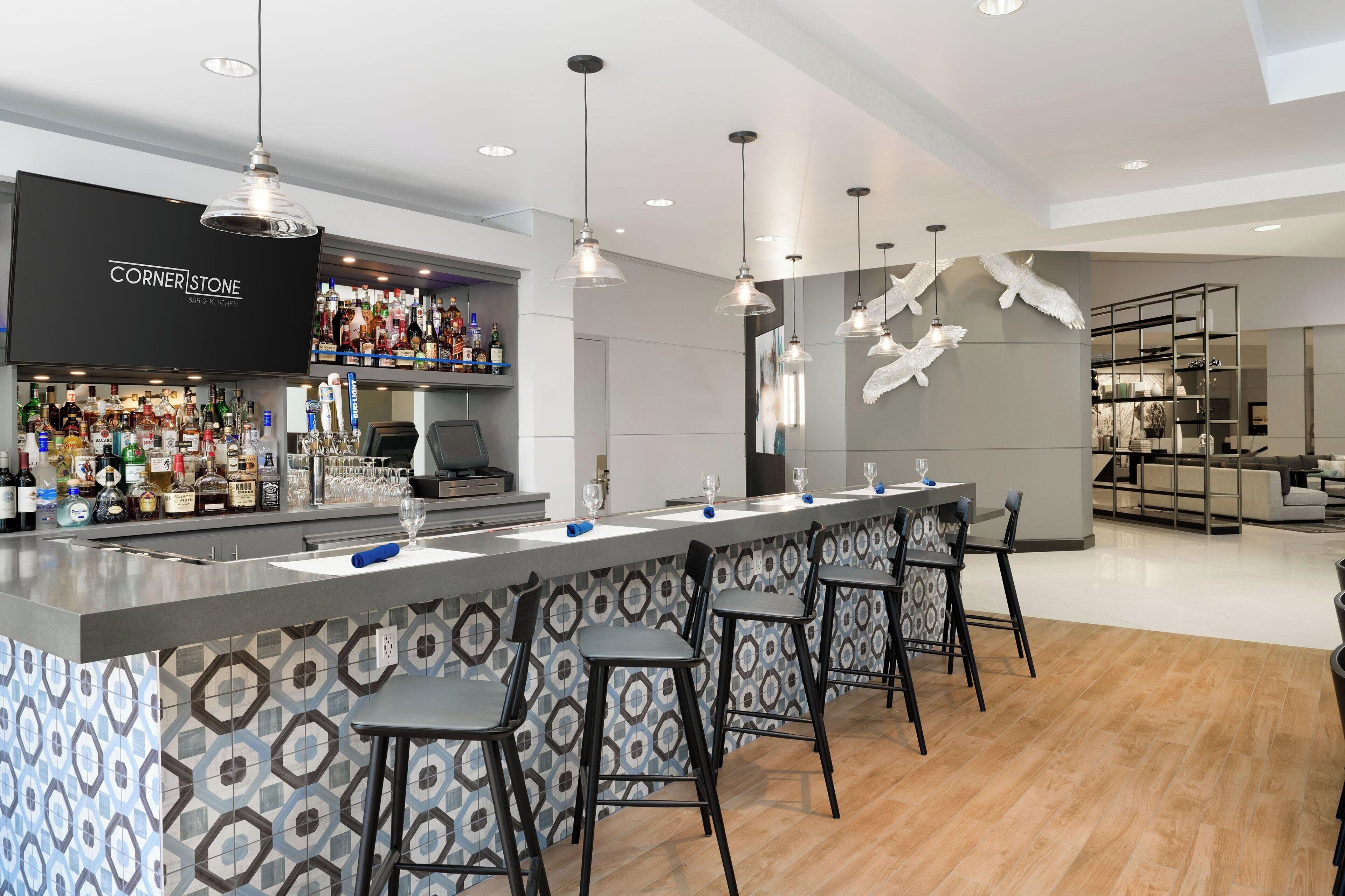 A modern bar area with a long counter, bar stools, and a variety of liquor bottles.