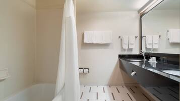 A modern bathroom with a bathtub, two sinks, a large mirror, and multiple towels on the wall.