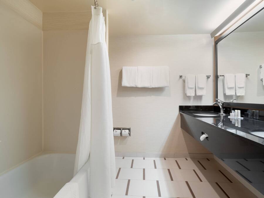 A modern bathroom with a bathtub, two sinks, a large mirror, and multiple towels on the wall.