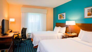 A hotel room with two beds, a desk with a computer, a chair, a TV, and a window with curtains.
