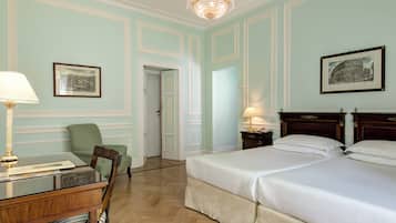 Habitación de hotel con dos camas, un escritorio con lámpara, una silla y cuadros en las paredes.