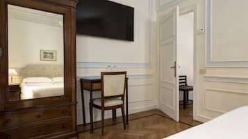 A hotel room with a wooden dresser, a desk with a chair, a flat-screen TV mounted on the wall, and a bed with white bedding.