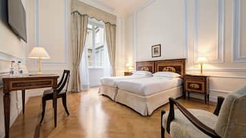 A hotel room with a double bed, two bedside tables with lamps, a desk with a chair, a TV mounted on the wall, and a window with curtains.