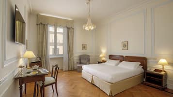 Une chambre d’hôtel avec un grand lit, un bureau avec une chaise, une chaise supplémentaire, une table de chevet avec une lampe et un lustre.