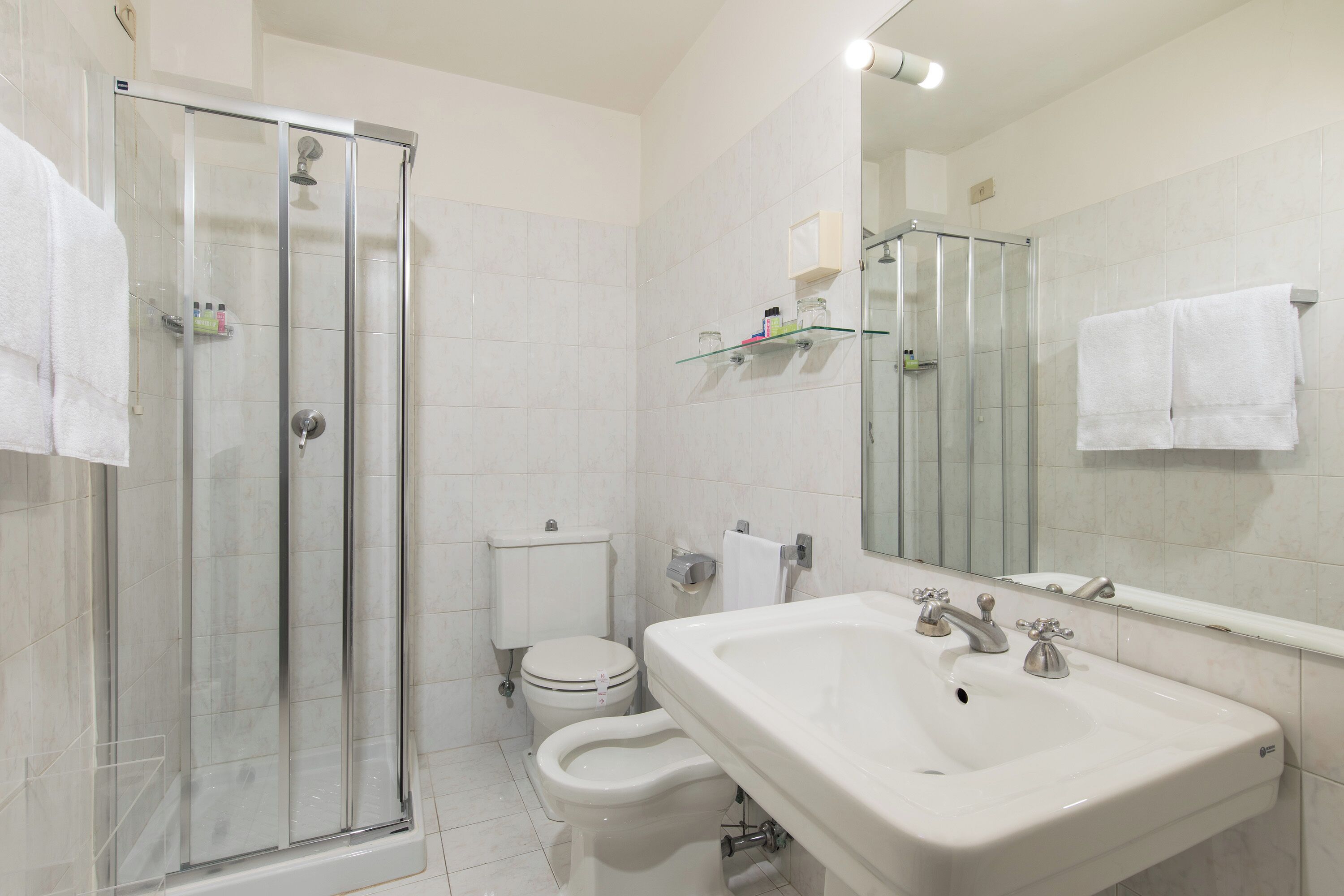 A bathroom with a glass-enclosed shower, a toilet, and a sink with a mirror above it.