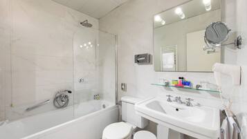 Un baño moderno con ducha de vidrio, inodoro blanco, lavamanos con espejo y artículos de tocador sobre la encimera.