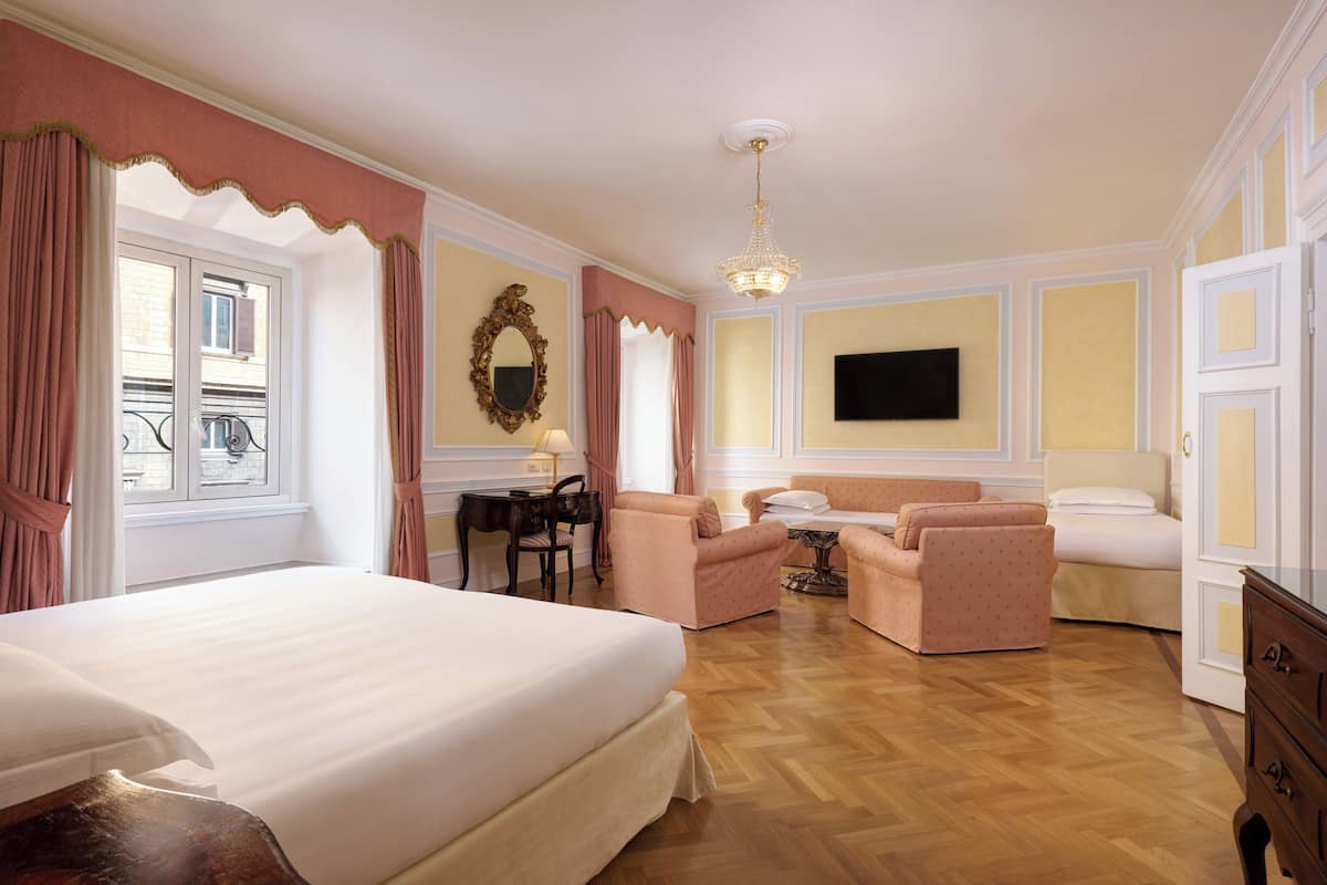 A hotel room with a large bed, two armchairs, a sofa, a small table, and a TV on the wall.