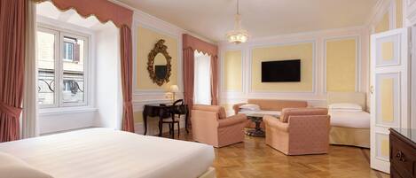 A hotel room with a large bed, two armchairs, a sofa, a small table, and a TV on the wall.
