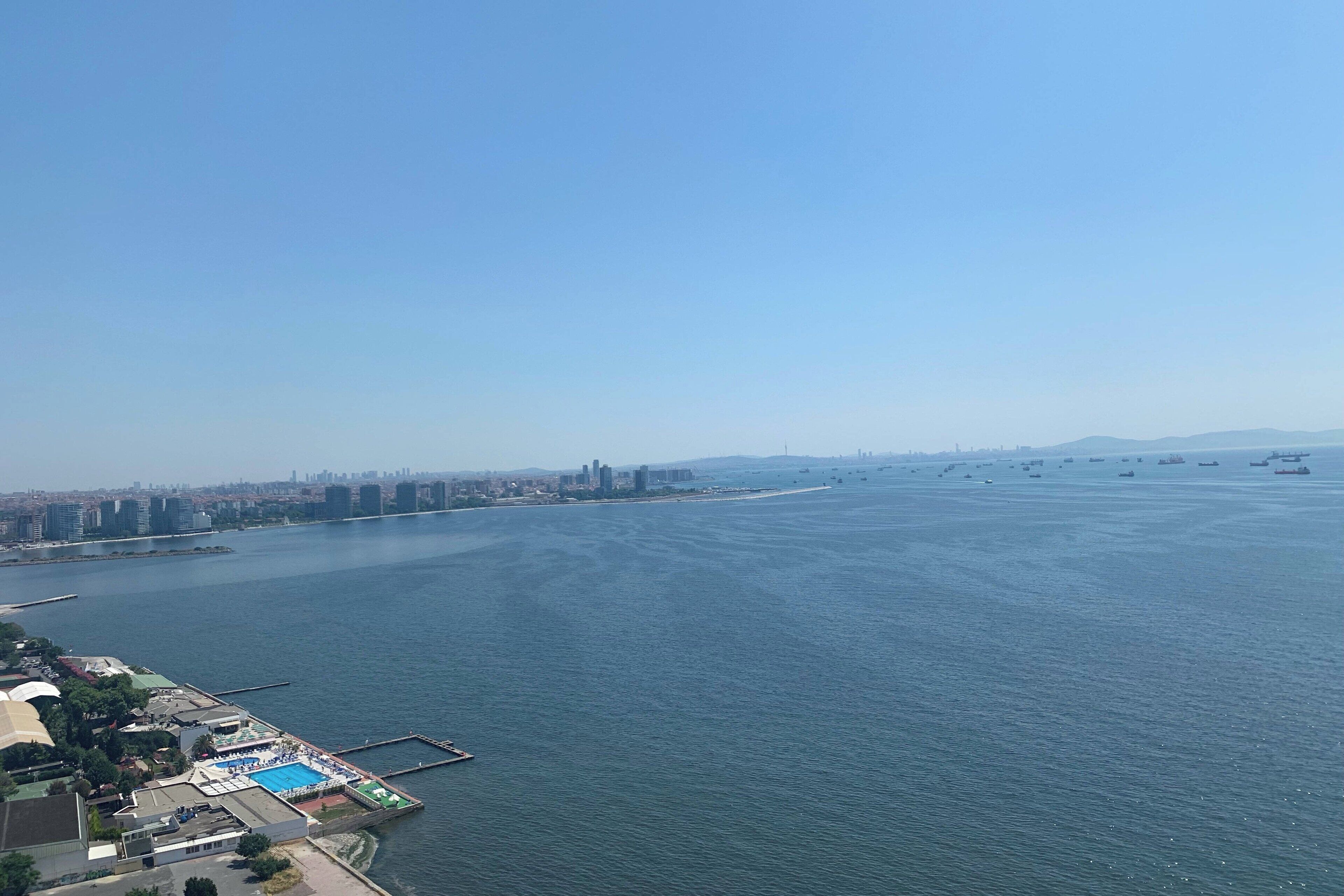 A waterfront property with a swimming pool, dock, and city skyline in the background.