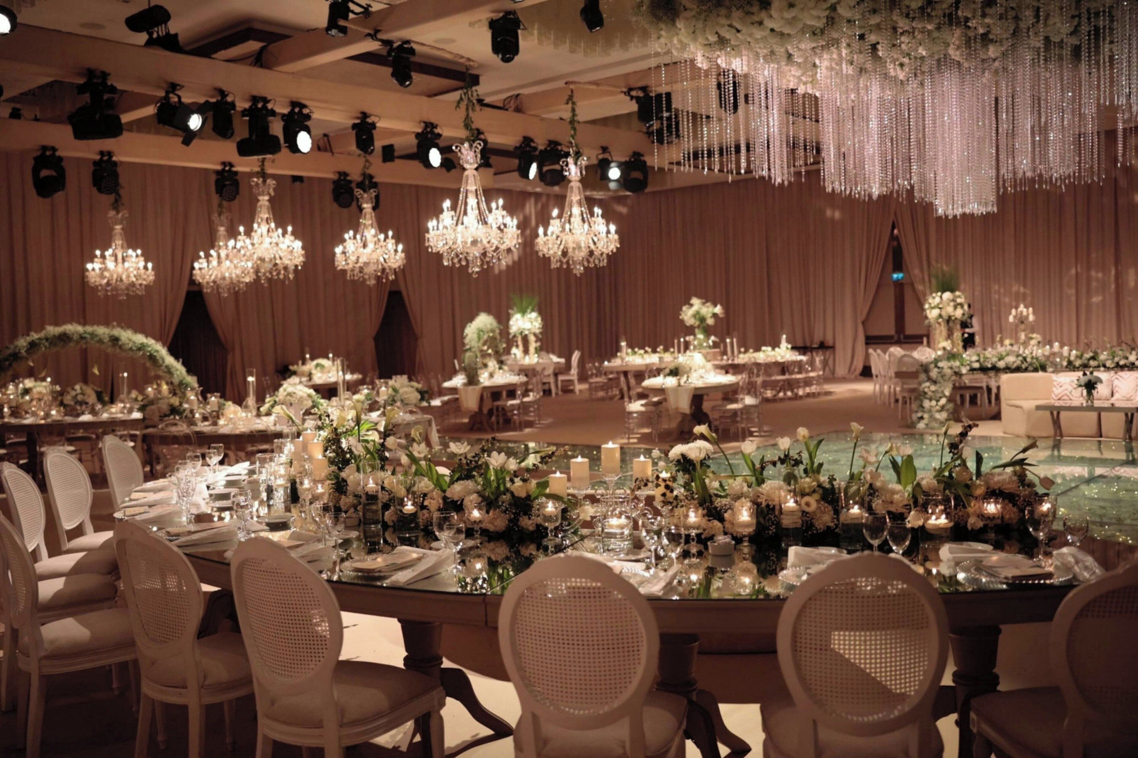 A banquet hall with multiple tables set for dining, chandeliers, and draped curtains.