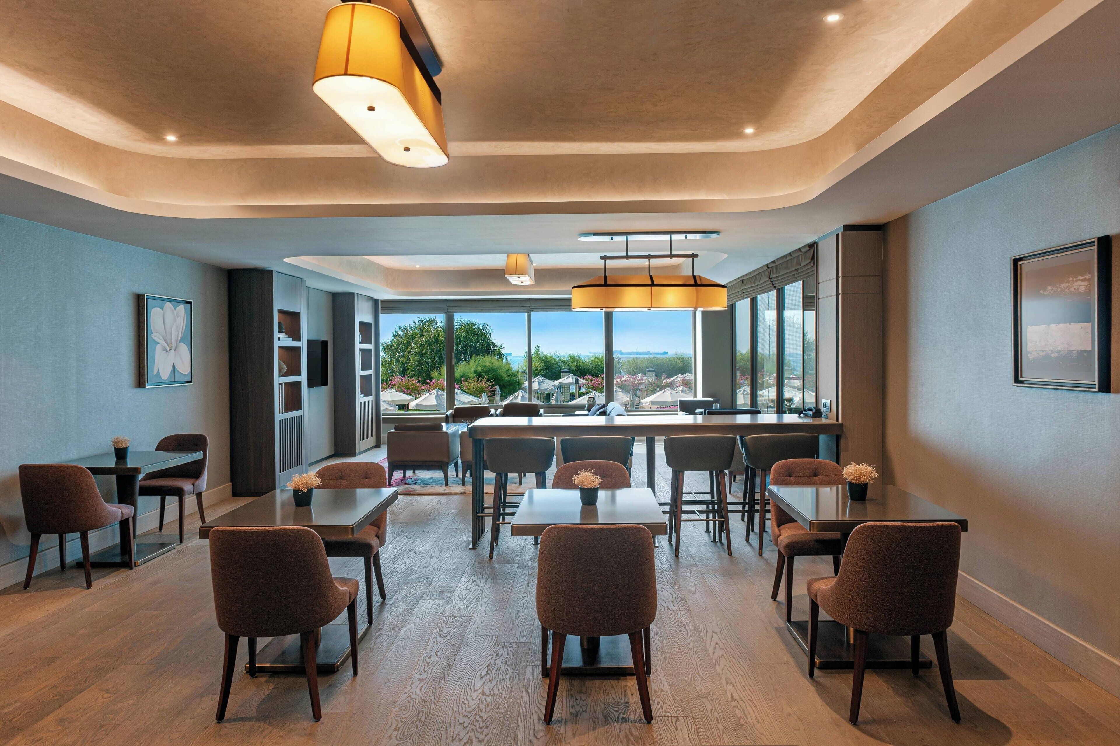 Un salón de conferencias moderno con una gran mesa y sillas, ventanas amplias con vistas, e iluminación colgante.