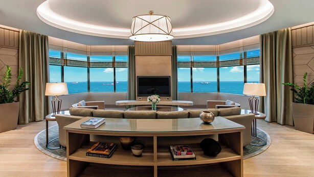 A modern living room with a circular glass coffee table, comfortable seating, a flat-screen TV, and large windows offering a view of the sea. - Renaissance Polat Istanbul Hotel (Istanbul)