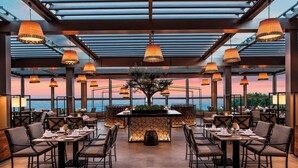 A restaurant with tables set for dining, a central bar area, and a view of the sea. - Renaissance Polat Istanbul Hotel (Istanbul)