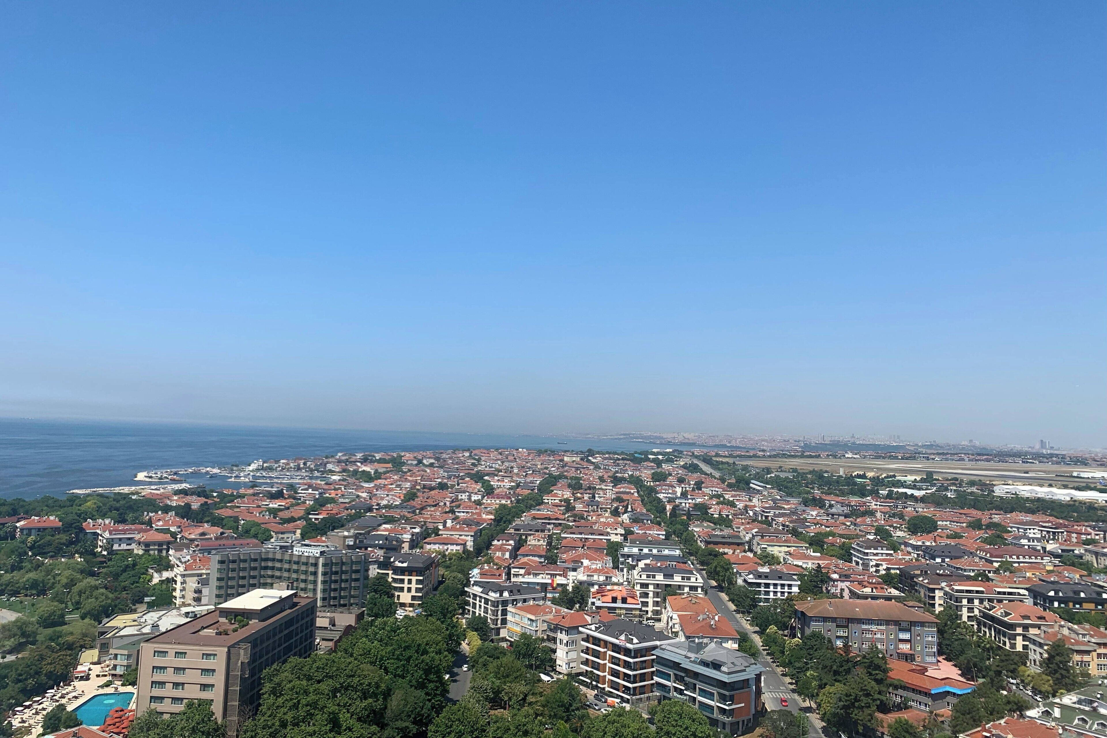 A cityscape with a view of the sea, featuring densely packed buildings with red roofs and a clear blue sky.