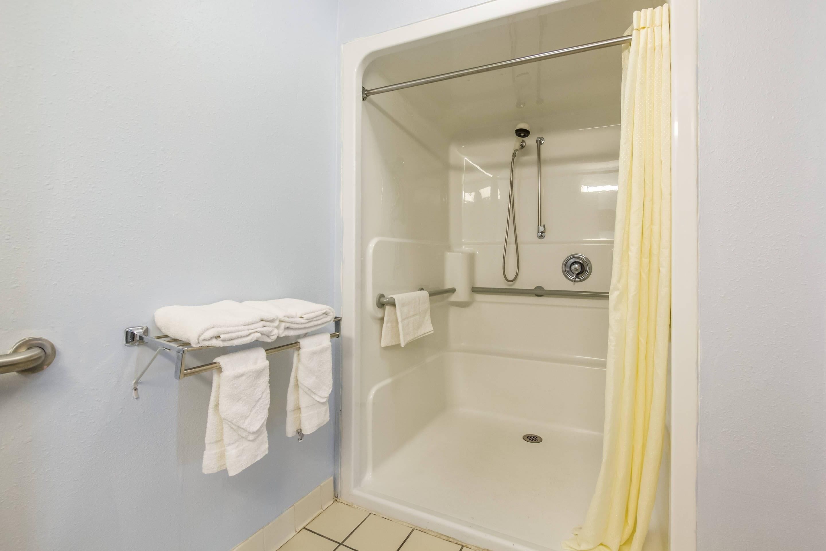 A walk-in shower with a glass door, a towel rack with folded towels, and a yellow shower curtain.
