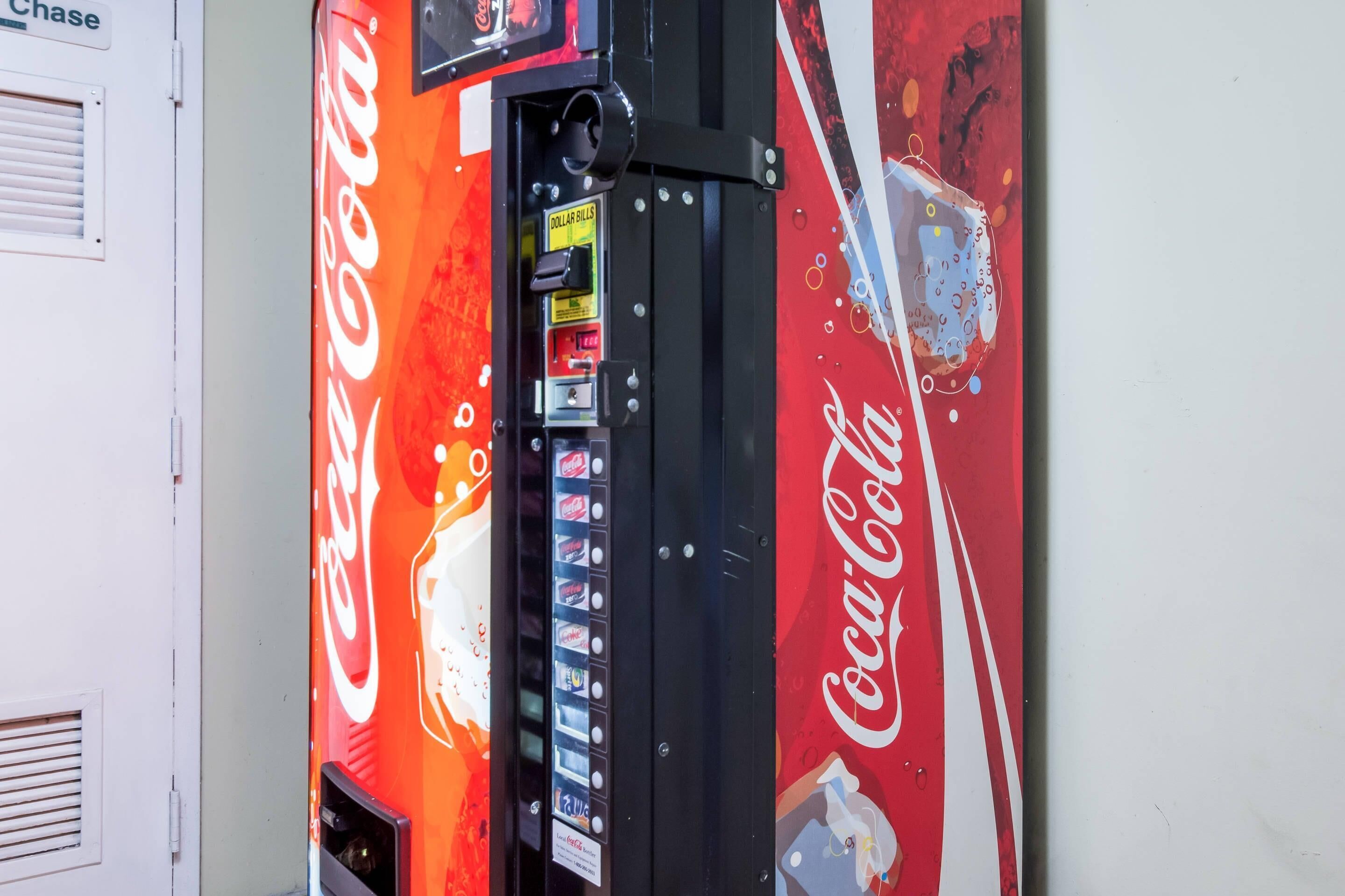 A Coca-Cola vending machine with a red and white design, a cash slot, and a selection of beverages.