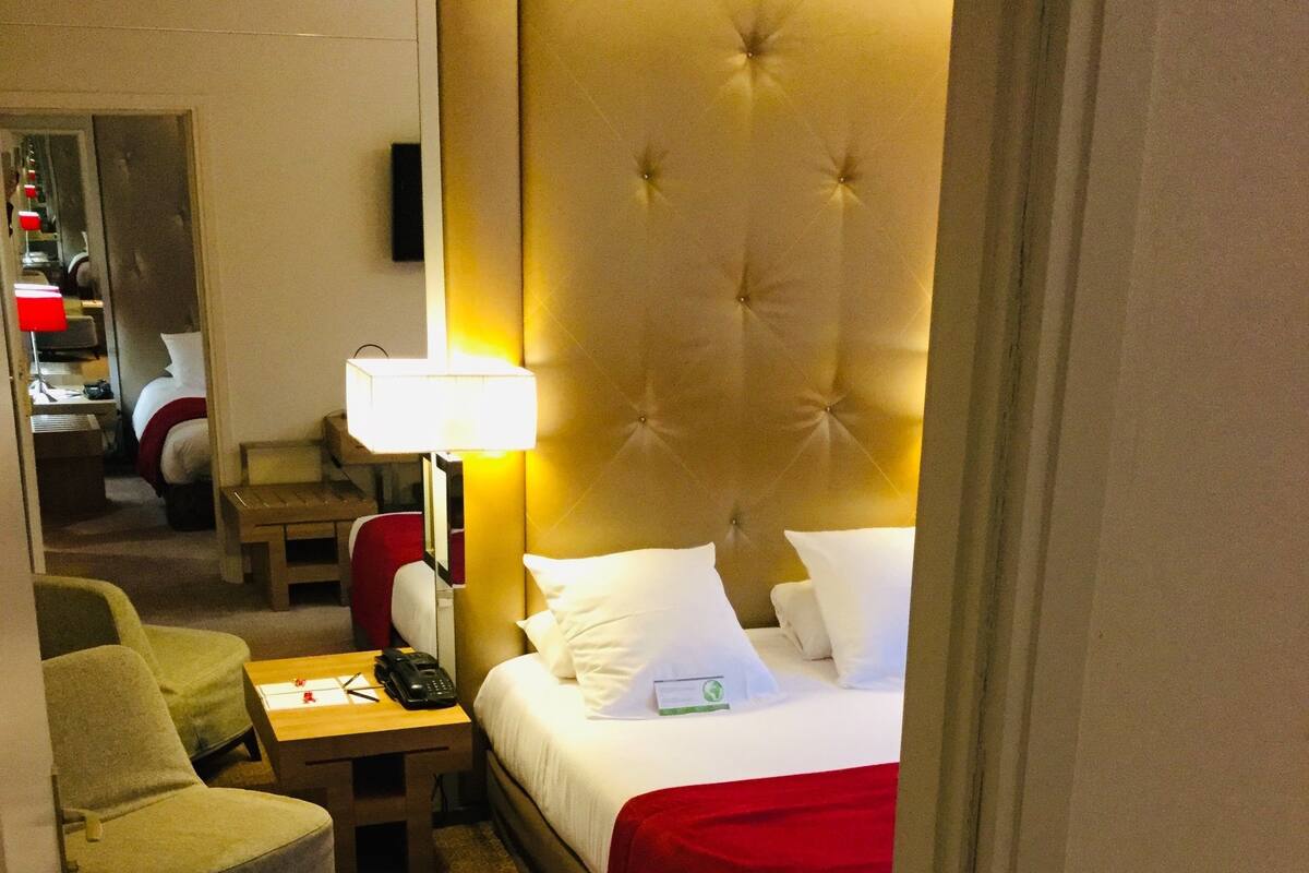 A hotel room with a bed, a bedside table, a lamp, a chair, and a small table.
