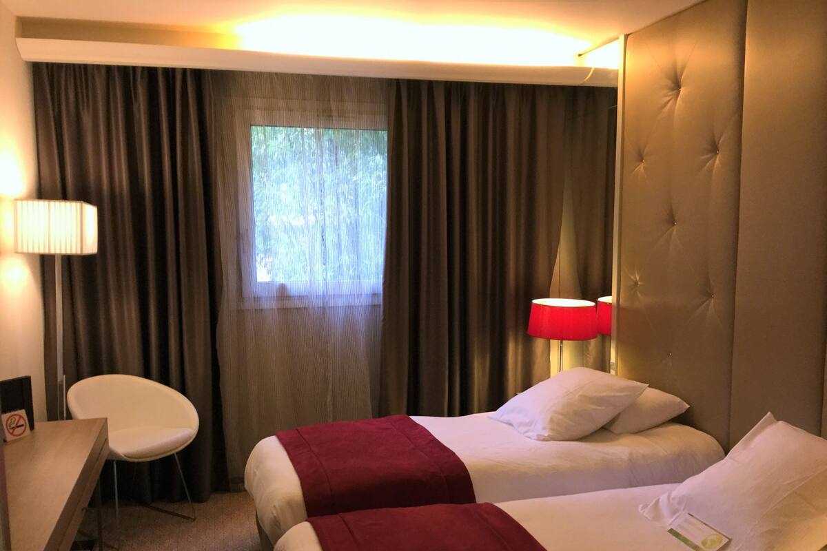 A hotel room with two beds, a desk, a chair, and a window with curtains.