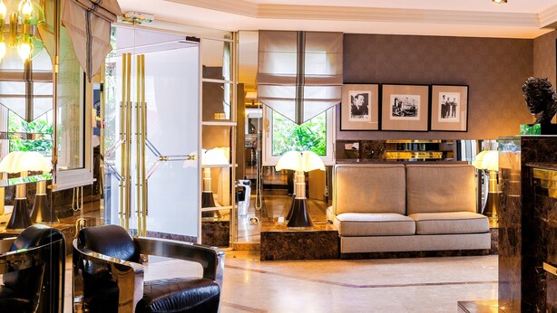 A modern living room with a sofa, chairs, and a coffee table. There are framed pictures on the wall and a sculpture on a pedestal. - Hôtel Mermoz (Toulouse)