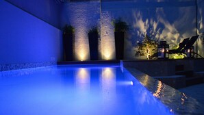 A swimming pool with a blue-lit edge, surrounded by a stone wall and potted plants. - Hôtel Mermoz (Toulouse)