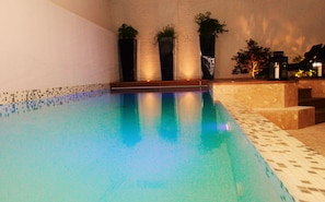 A swimming pool with a tiled edge, surrounded by walls and a stone bench. - Hôtel Mermoz (Toulouse)