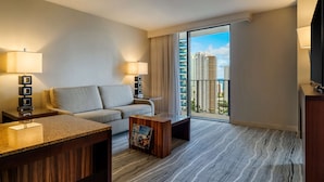 Una habitación de hotel moderna con un sofá, una mesa de centro y un televisor. La habitación tiene un ventanal con vistas a edificios altos.