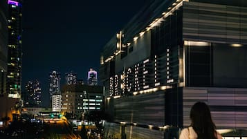 Un edificio moderno con un letrero iluminado grande, rodeado de edificios altos y una calle concurrida por la noche.