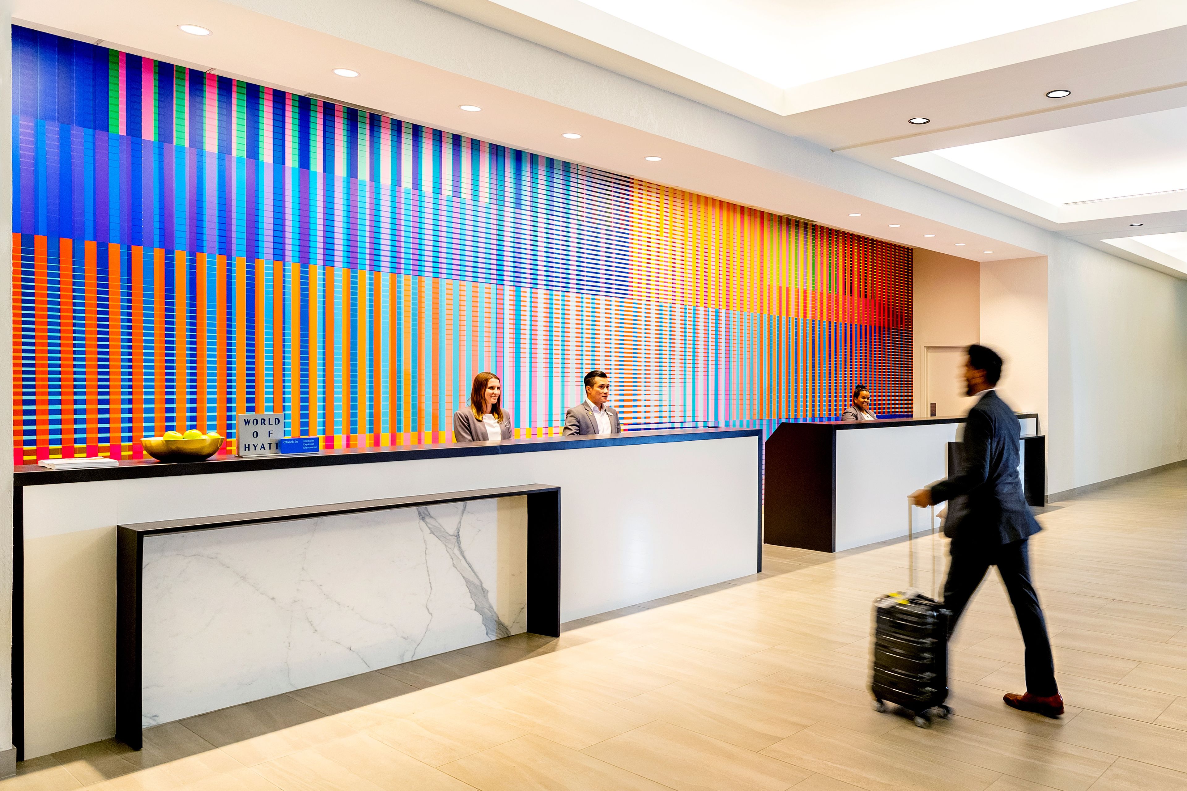 A hotel reception desk with a modern design, a marble counter, and a colorful vertical panel in the background.