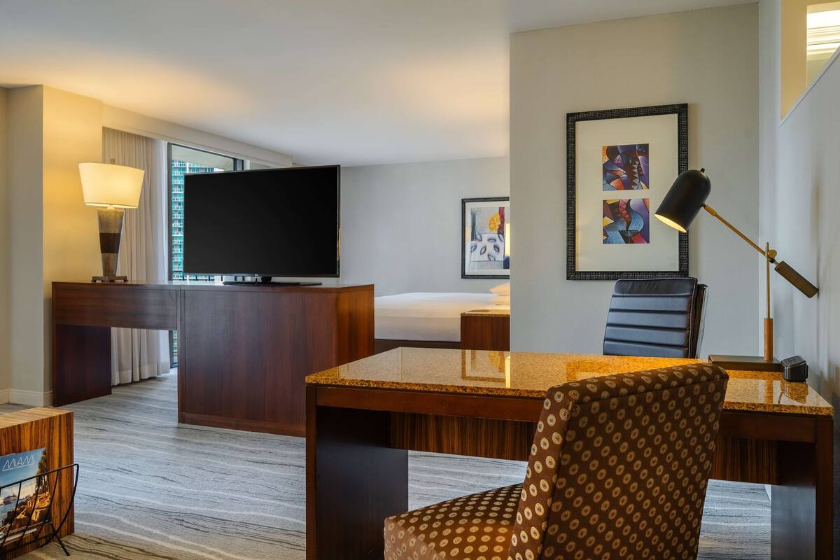 A hotel room with a bed, a desk with a chair, a television, and artwork on the wall.