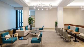 A modern lounge area with sofas, armchairs, and tables, featuring a geometric patterned carpet and a contemporary light fixture.