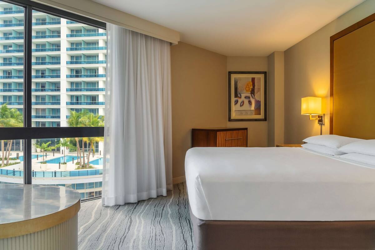 A hotel room with a large bed, a desk, a chair, a lamp, and a painting on the wall.