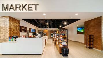A modern market interior with a reception desk, shelves stocked with products, and a sign indicating a grab-and-go area.