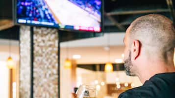 Een man zittend aan de bar, met daarboven een televisie, die een glas vasthoudt.