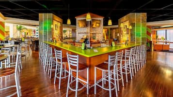 Zona de bar con una barra alargada y varios taburetes, en un ambiente moderno con techos altos y suelo de madera.