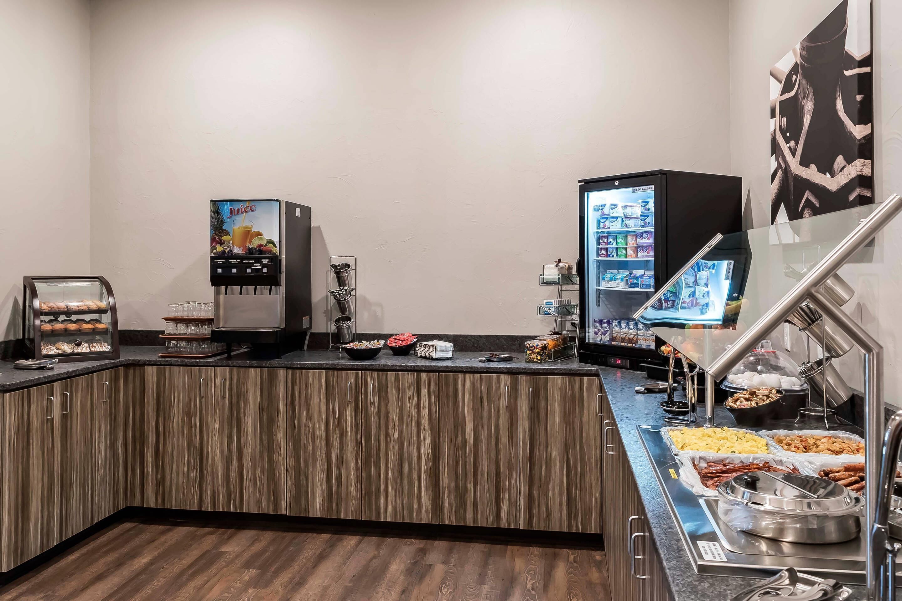 Un área de bufé con dispensador de jugos, un refrigerador y una pantalla digital con el menú.