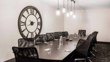 A conference room with a large clock, black leather chairs, a long table, and hanging lights.