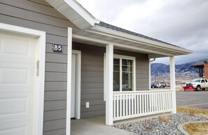 A residential building with a grey siding exterior, a white front door, and a porch with a white railing.