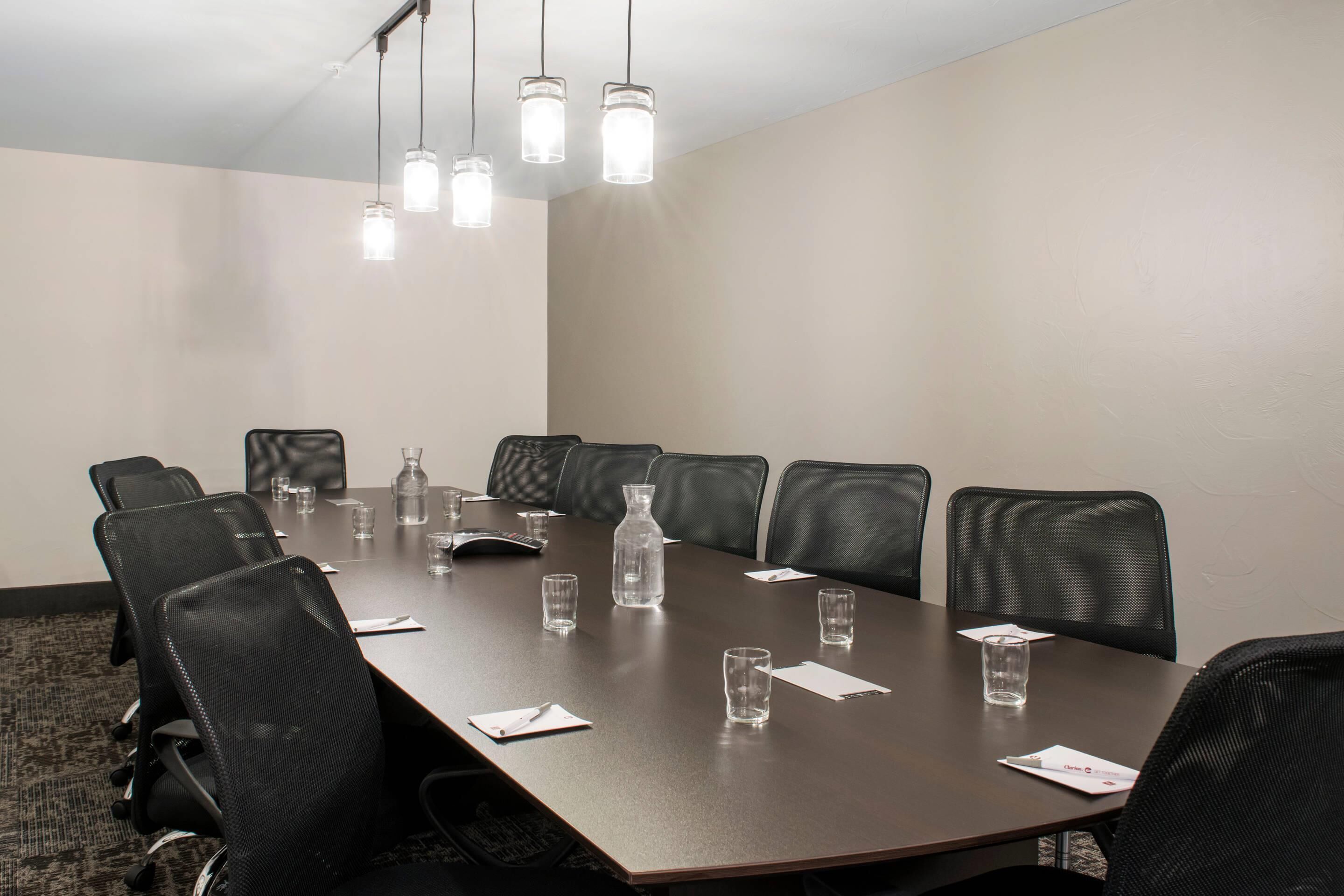 A conference room with a long table, black leather chairs, and hanging pendant lights.