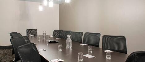 A conference room with a long table, black leather chairs, and hanging pendant lights.