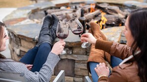 Three people sitting by a stone fire pit, holding wine glasses. - Copper King Convention Center, an Ascend Collection Hotel (Butte)