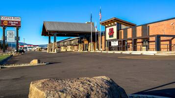 A parking lot with a large rock in the foreground, a building with a sign for 'Copper King Convention Center' and 'Clarion Inn', and an American flag.