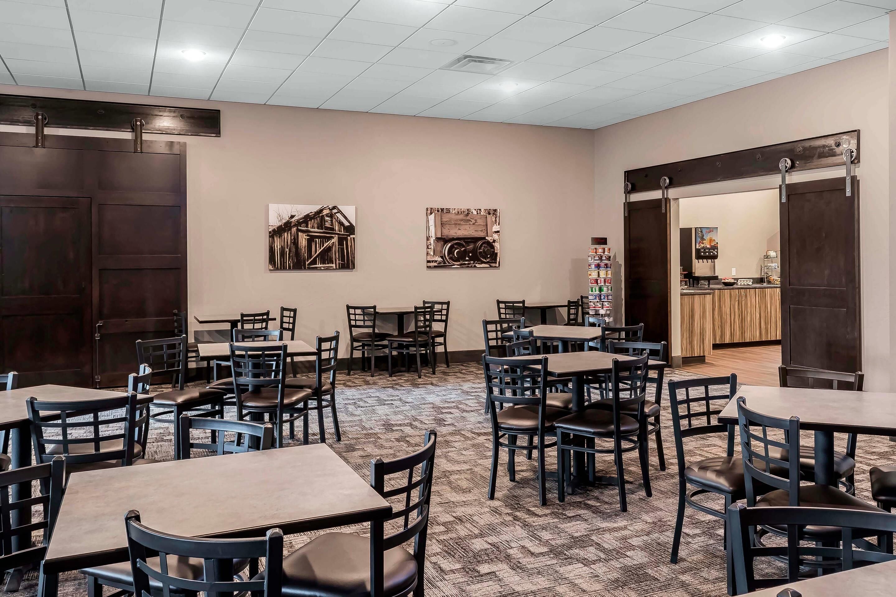 A hotel dining area with multiple tables and chairs, wooden doors, and framed pictures on the walls.