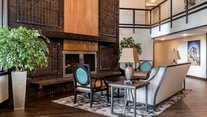 A spacious lobby with a large plant, a fireplace, and a seating area with a sofa and chairs. - Copper King Convention Center, an Ascend Collection Hotel (Butte)