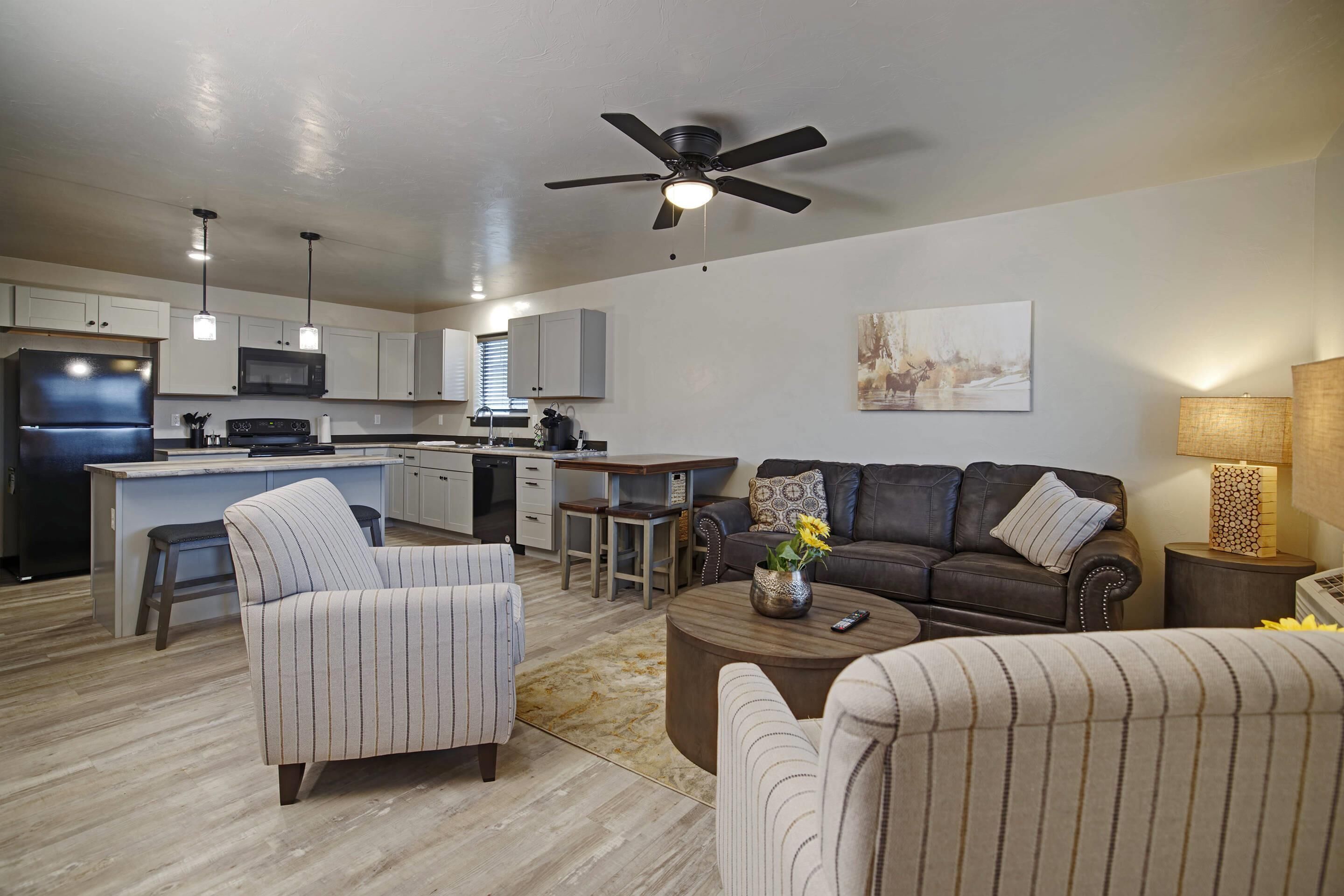 A modern kitchen with a central island, a dining area with a sofa and coffee table, and a living room with a couch and a painting on the wall.