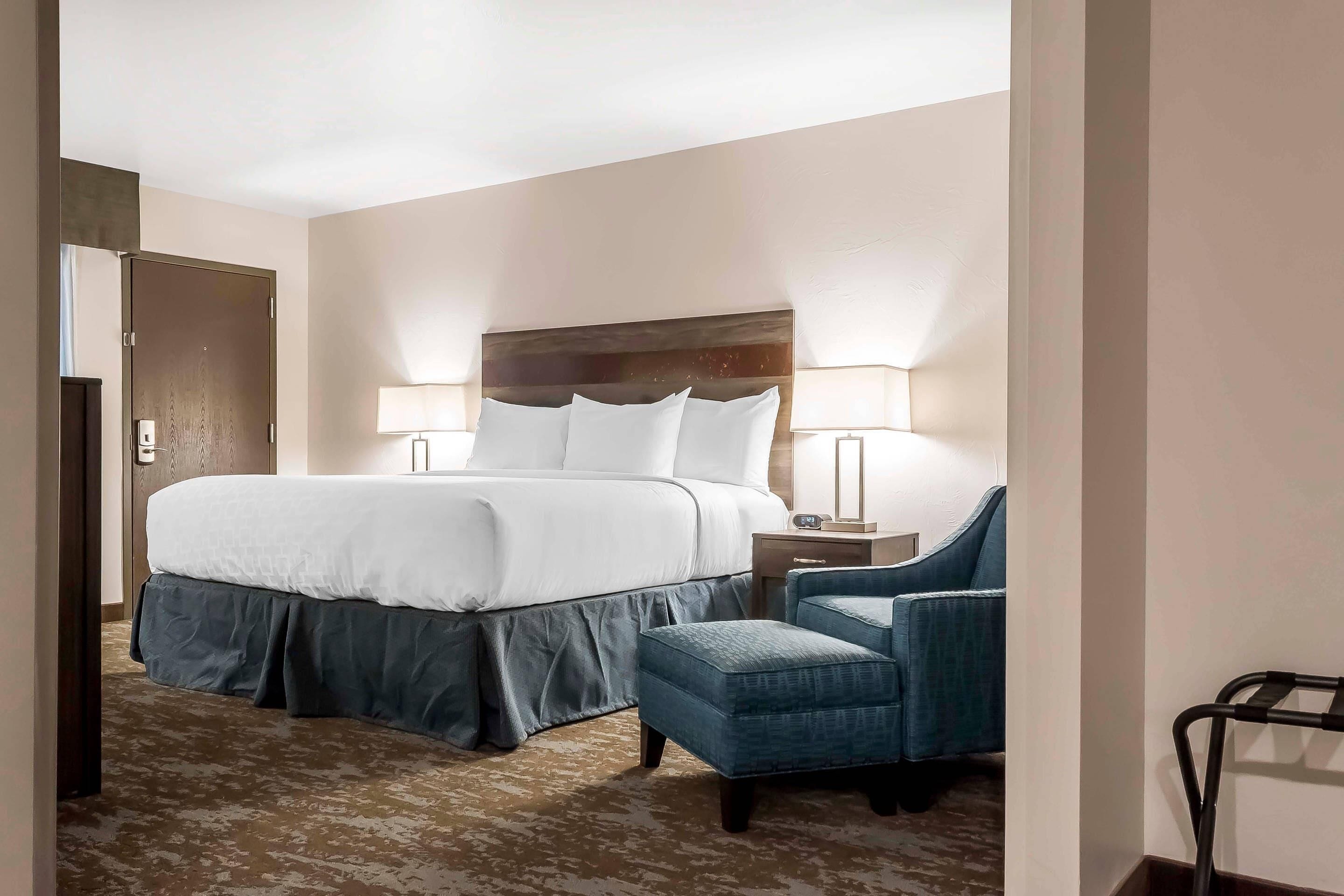 Quarto de hotel com uma cama grande, uma escrivaninha com luminária e uma cadeira.
