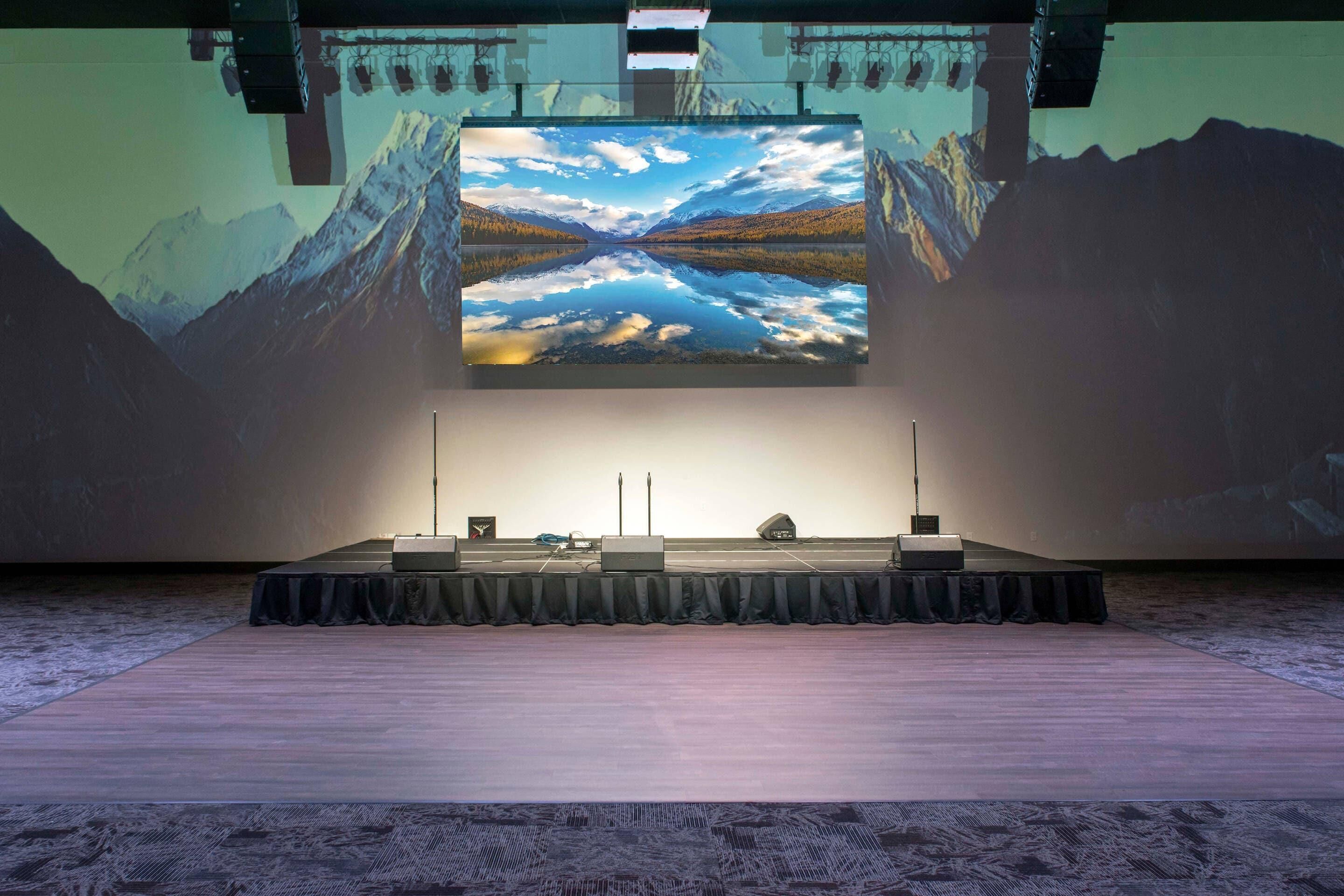 Eine Präsentationsbühne mit einer großen Leinwand, die eine Berglandschaft zeigt, einem Rednerpult und einem Mikrofonständer.